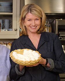 two people standing in a kitchen holding a pie with whipped cream on the top and bottom