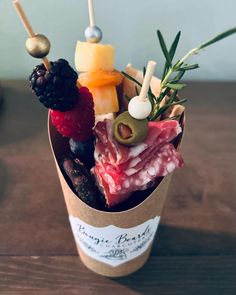 a cup filled with assorted meats and cheese on top of a wooden table