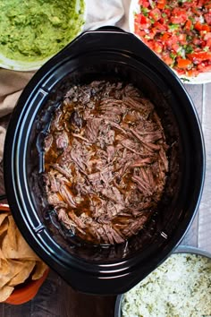 a crock pot filled with shredded beef and salsa next to tortilla chips