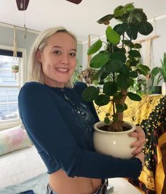 a woman is holding a potted plant in her hands and smiling at the camera