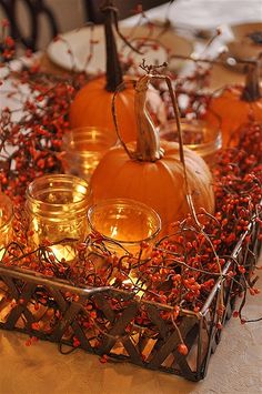 candles and pumpkins are arranged in a basket on a table with red berries around them