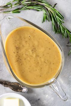 a glass bowl filled with gravy on top of a table next to cheese