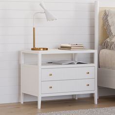 a white nightstand with a book on it next to a bed