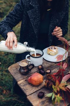 a person pouring milk into a cup on top of a wooden table next to fruit