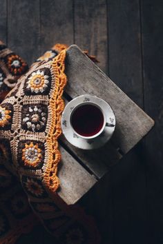 a cup of tea on top of a wooden table next to a crocheted blanket