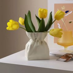 yellow tulips in a white vase on a table next to magazines and magazine