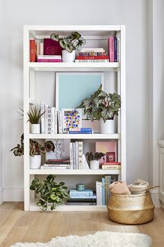 a white book shelf filled with books and plants