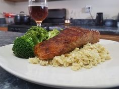 a plate with rice, broccoli and meat on it next to a glass of wine