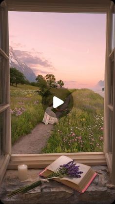 an open window with a book and flowers in front of it, looking out onto a field