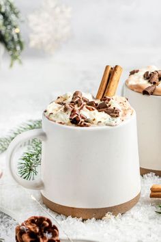 two white mugs filled with hot chocolate and whipped cream, topped with cinnamon sticks