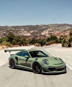 a green sports car driving down a road with mountains in the backgrouund