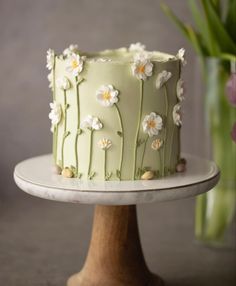 a green cake with white flowers on it sitting on a plate next to a vase