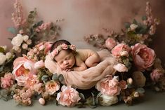 a newborn baby is sleeping in a pink blanket surrounded by flowers and greenery on a gray background