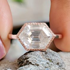 a close up of a person's hand touching an engagement ring on top of a rock