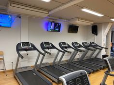 there are many treadmills in the gym with monitors on the wall behind them