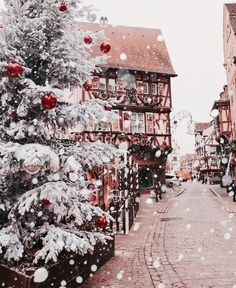 a christmas tree in the middle of an old town street with snow falling on it