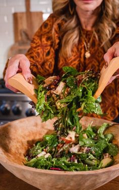 a woman is mixing a salad in a wooden bowl