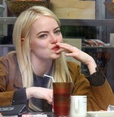 a blonde haired woman sitting at a table with a drink in her hand and looking off to the side