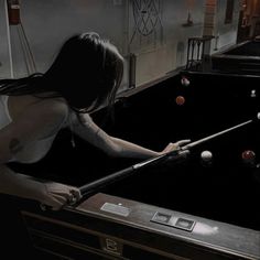 a woman is playing pool in a dark room