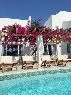 lounge chairs next to a swimming pool with pink flowers growing on the wall and roof