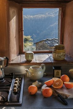 there are oranges and tea pots on the counter in front of an open window