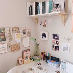 a white desk topped with lots of books next to a wall filled with pictures and papers