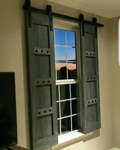 an open window with shutters in front of a flat screen tv mounted on a wall