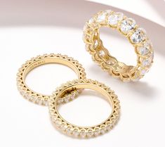 three different types of gold rings on a white surface, one with clear crystal stones