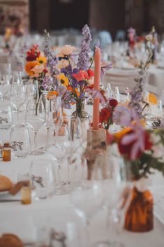 the table is set with wine glasses, candles and flowers in vases on it