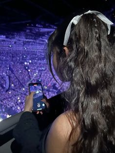 a woman is looking at her cell phone in front of a large screen with purple lights