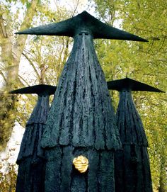 a sculpture in the middle of a park with trees around it and two birds on top