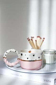 a pink cup with hearts on it sitting next to some matchesticks and a jar