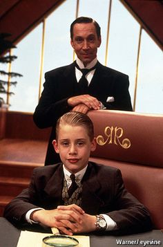 a young boy sitting at a desk in front of an older man wearing a suit