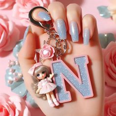 a hand holding a key chain with a doll and letter n on it, surrounded by pink roses