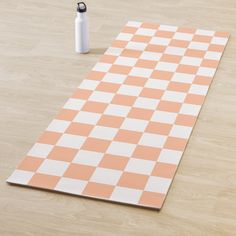 an orange and white checkered rug next to a water bottle on a wooden floor