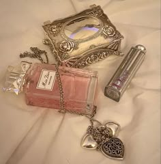 two perfume bottles and a necklace laying on a white sheet with a silver purse next to it