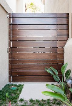 a wooden gate in front of a house with grass on the ground and potted plants next to it