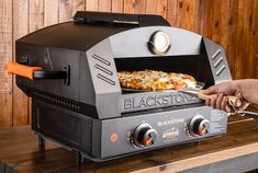 a person is pulling a pizza out of an outdoor grill