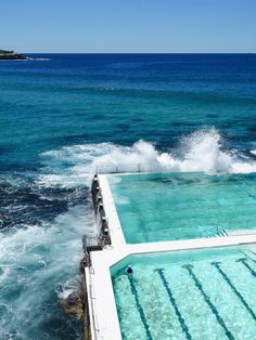 an outdoor swimming pool with clear blue water and waves coming in from the ocean on a sunny day