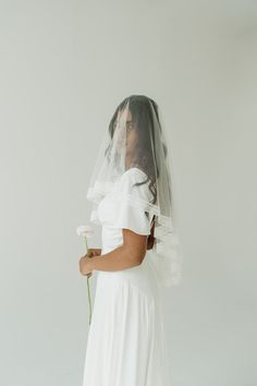 a woman wearing a veil and holding a flower in her hand while standing against a white background