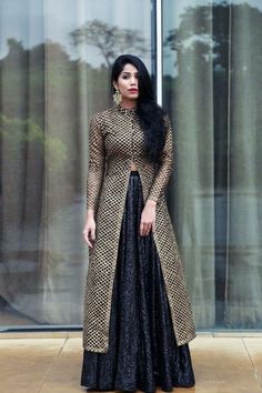 a woman standing in front of a window wearing a black and gold dress with long sleeves