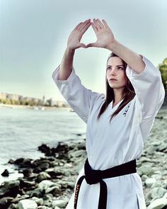 a woman in a white kimono standing on rocks by the water holding her hands up