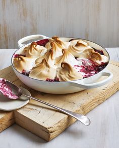 a dish filled with dessert sitting on top of a wooden cutting board next to two spoons