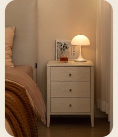 a nightstand with a lamp on top of it next to a bed