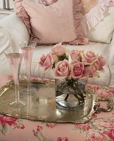 pink roses in a glass vase on a tray next to two wine glasses and a silver tray