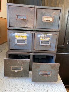 four metal drawers with labels on them sitting on top of a white counter next to a wooden cabinet