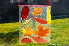 a bird feeder hanging from the side of a window in front of a house with autumn leaves painted on it