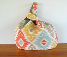 an orange, yellow and blue fabric bag sitting on top of a wooden table next to a white wall