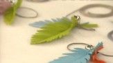 three different colored feathers sitting on top of a white table next to rings and beads