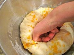 someone is kneading an uncooked pizza dough into a metal mixing bowl